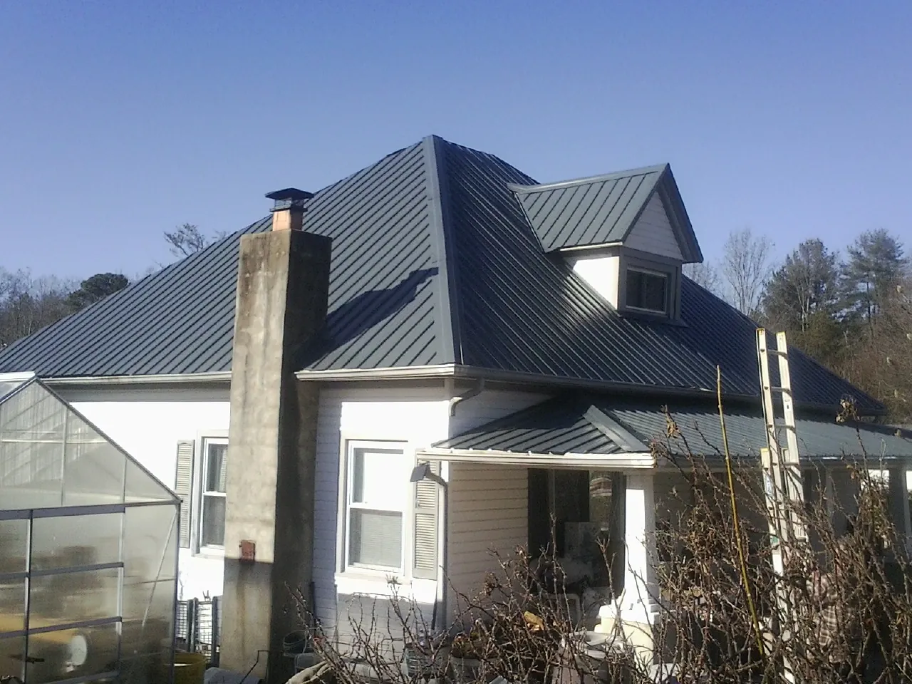 Dark blue standing seam metal roof on a white farmhouse with dormer — Slate & Tile Roof Repair by Roofing Brothers in Kenly