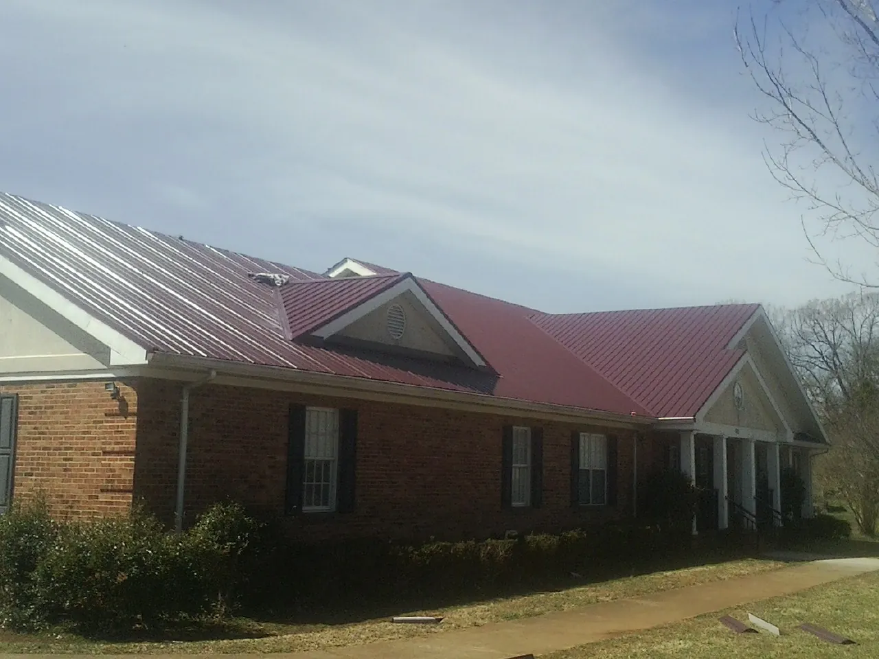 Red metal roof with gabled entries on a long brick building, from a Hail Damage Roof Repair job in Kenly