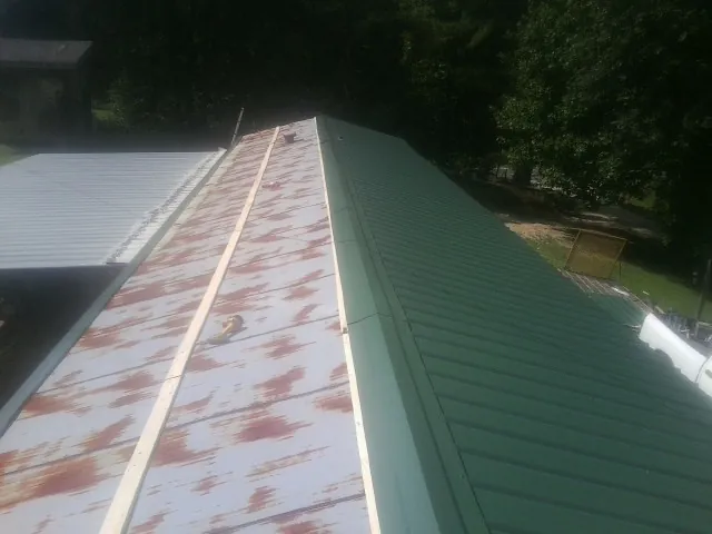 Old rusted panels beside newly installed green metal roofing — Wind Damage Roof Repair by Roofing Brothers in Kenly