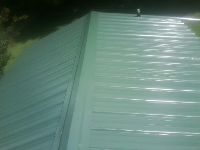 New green metal panels meeting at the ridge of a roof — Flat Roof Repair work by our crew in Kenly