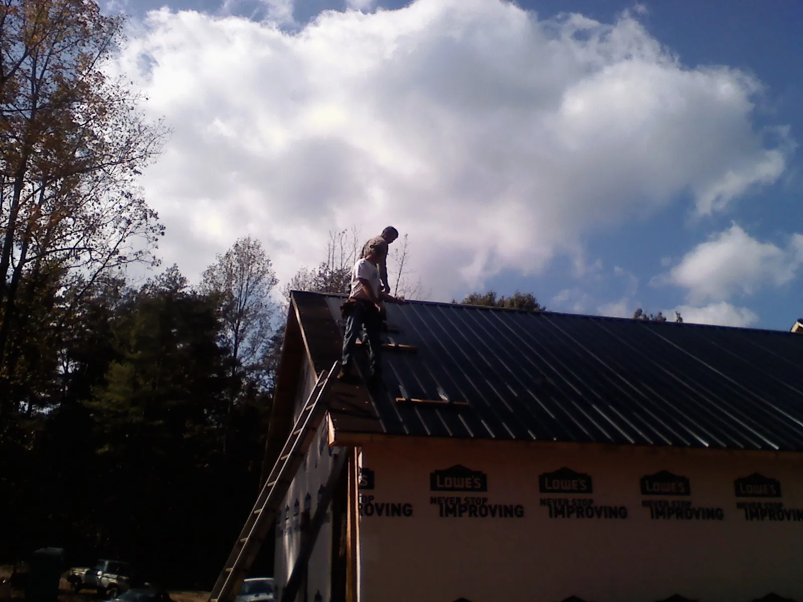 Roofer fastening dark metal panels high against a cloudy sky, from a Roof Inspection job in Kenly