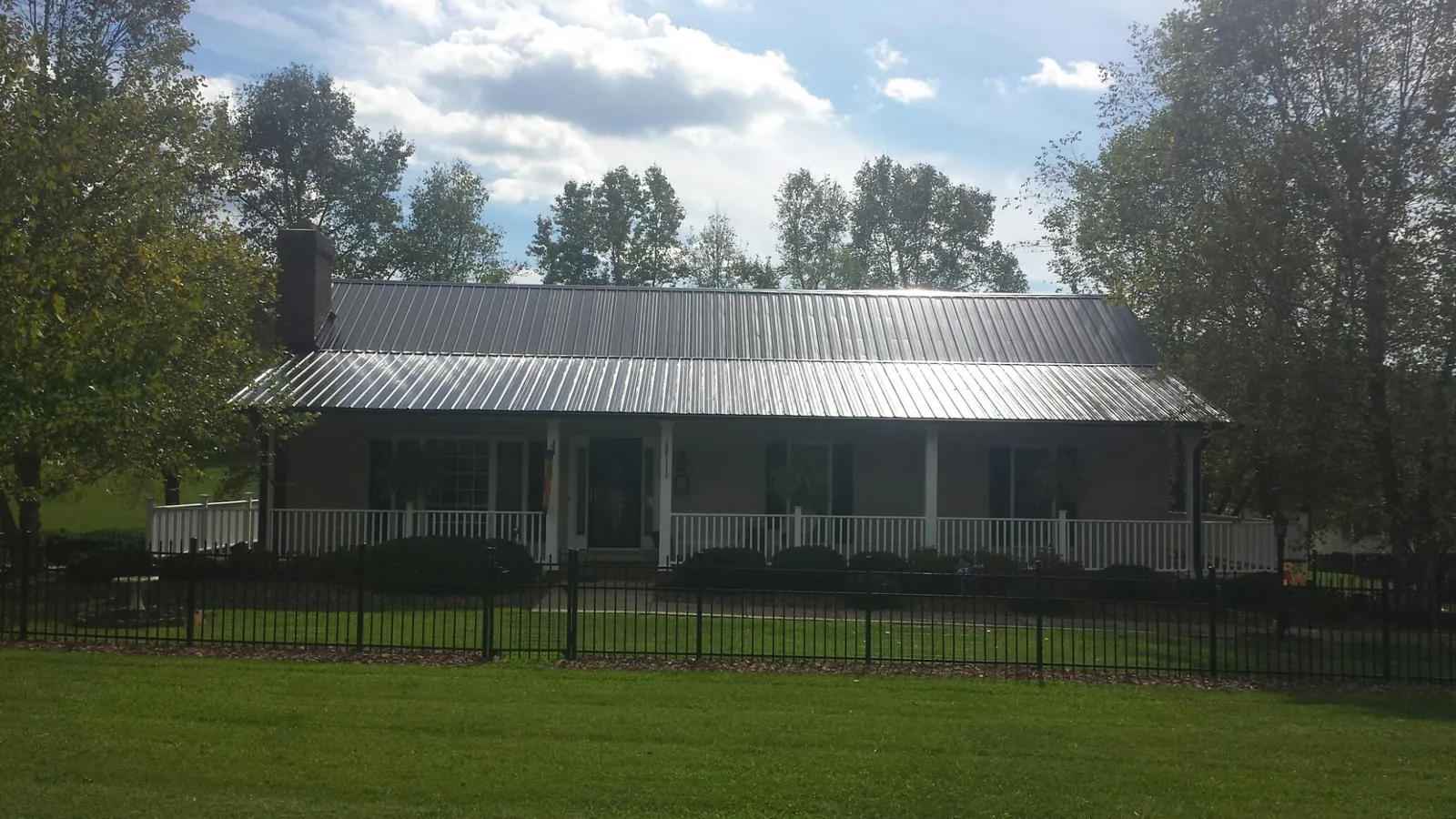 Gray metal roof on a brick ranch with a full width front porch — Gutter Guard Installation work by our crew in Kenly