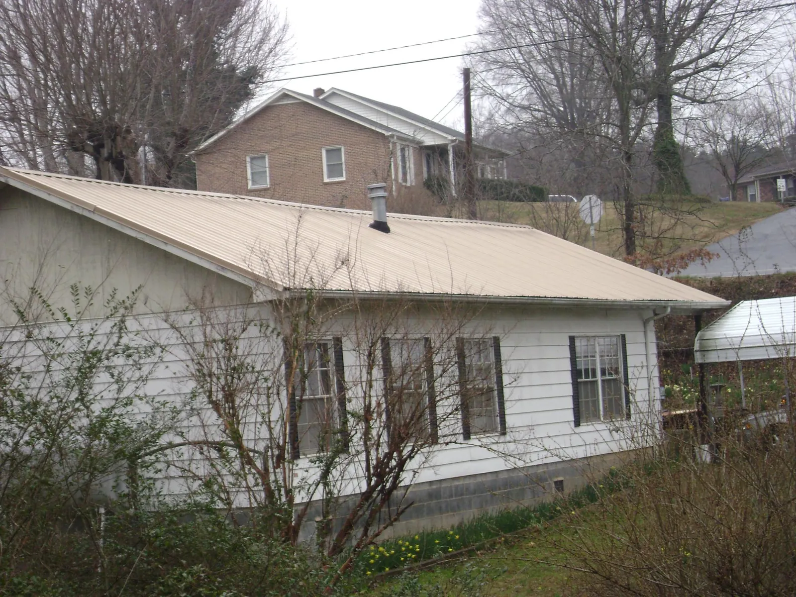 Tan metal roof on a white sided house set into a hillside — Commercial Roofing by Roofing Brothers in Kenly